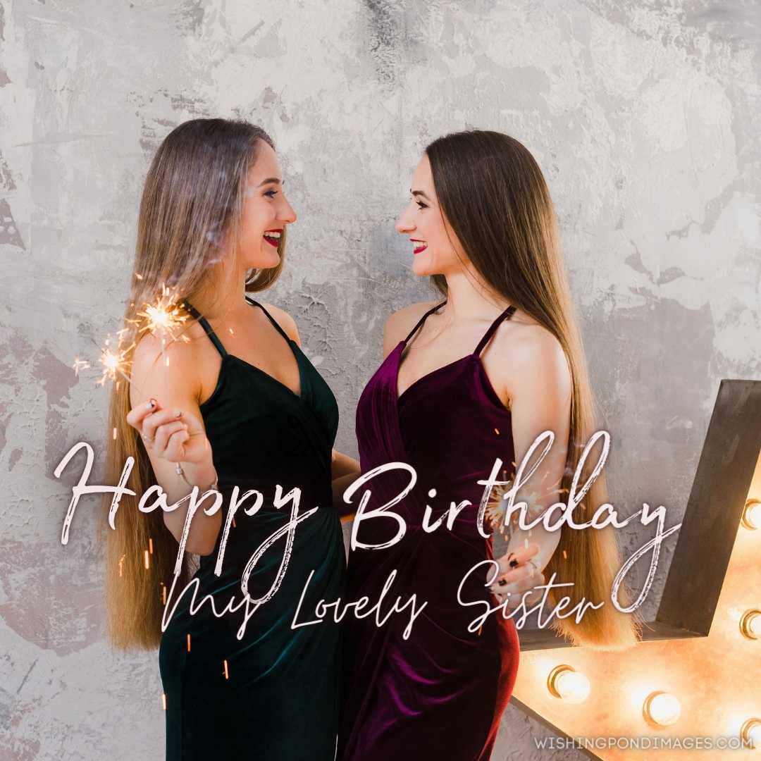 Beautiful smiling sisters with long hair in evening dress holding sparklers over Christmas. Happy Bi